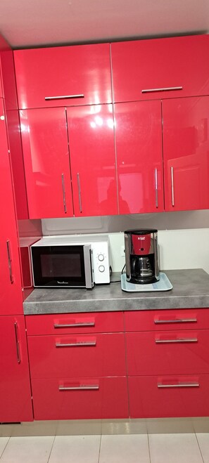 A kitchen with red cabinets, a microwave, and a coffee maker on the countertop. -  grande propriété close (Polisot)