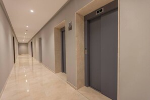 A corridor with a polished floor, doors, and a digital display above one of the doors. - Elegant 3BR Apartment - Gym, Terrace & Nice View (Tanger)