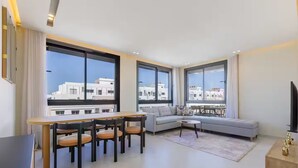 Un salon moderne avec un coin repas, de grandes fenêtres et un balcon offrant une vue sur la ville.