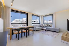 A modern living room with a dining area, large windows, and a balcony with a city view. - Elegant 3BR Apartment - Gym, Terrace & Nice View (Tanger)