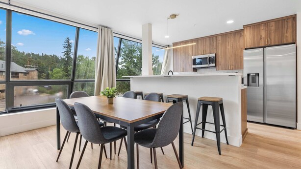 A modern kitchen with a built-in microwave, a stainless steel refrigerator, and a dining area with a wooden table and chairs.