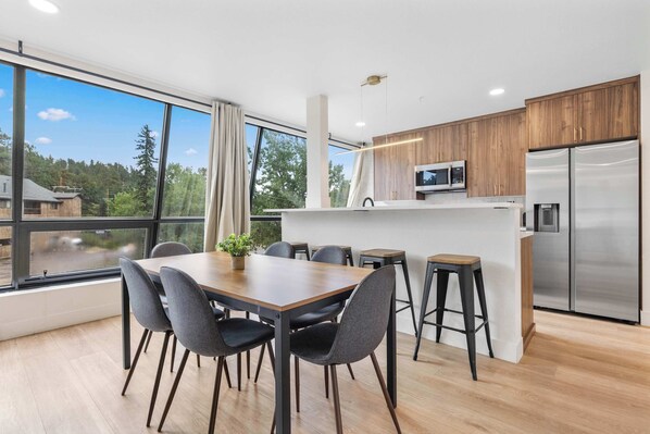 A modern kitchen with a built-in microwave, a stainless steel refrigerator, and a dining area with a wooden table and chairs.