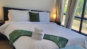 Ein Hotelzimmer mit einem großen Bett, einem Nachttisch, Vorhängen und einem gemusterten Teppich.