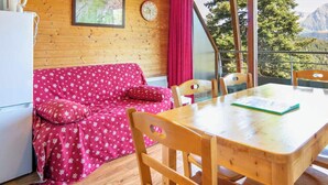 Ein Holzinterieur mit einem roten, gemusterten Sofa, einem Esstisch und Stühlen.