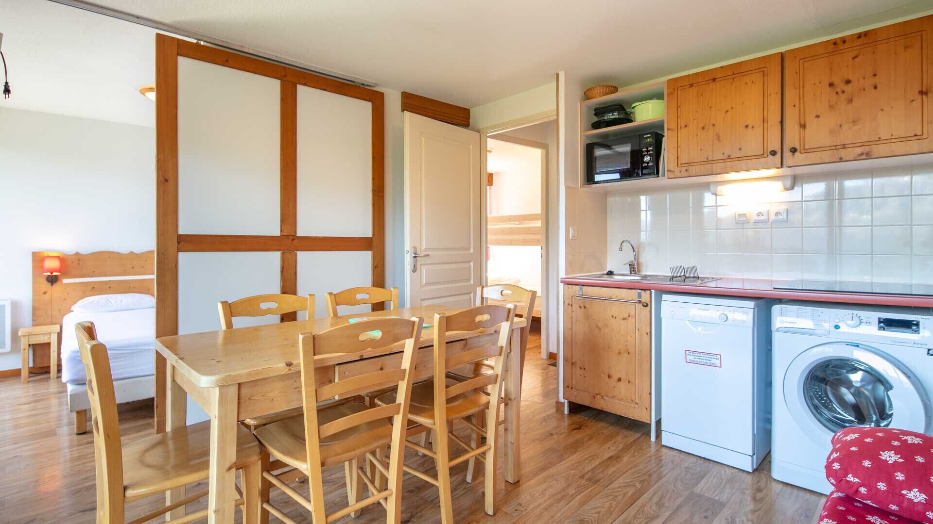 A compact kitchen with wooden cabinets, a washing machine, and a dining area with a table and chairs.