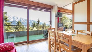 Ein Balkon mit Blick auf Berge, ein Esstisch mit Stühlen und ein Fernseher.
