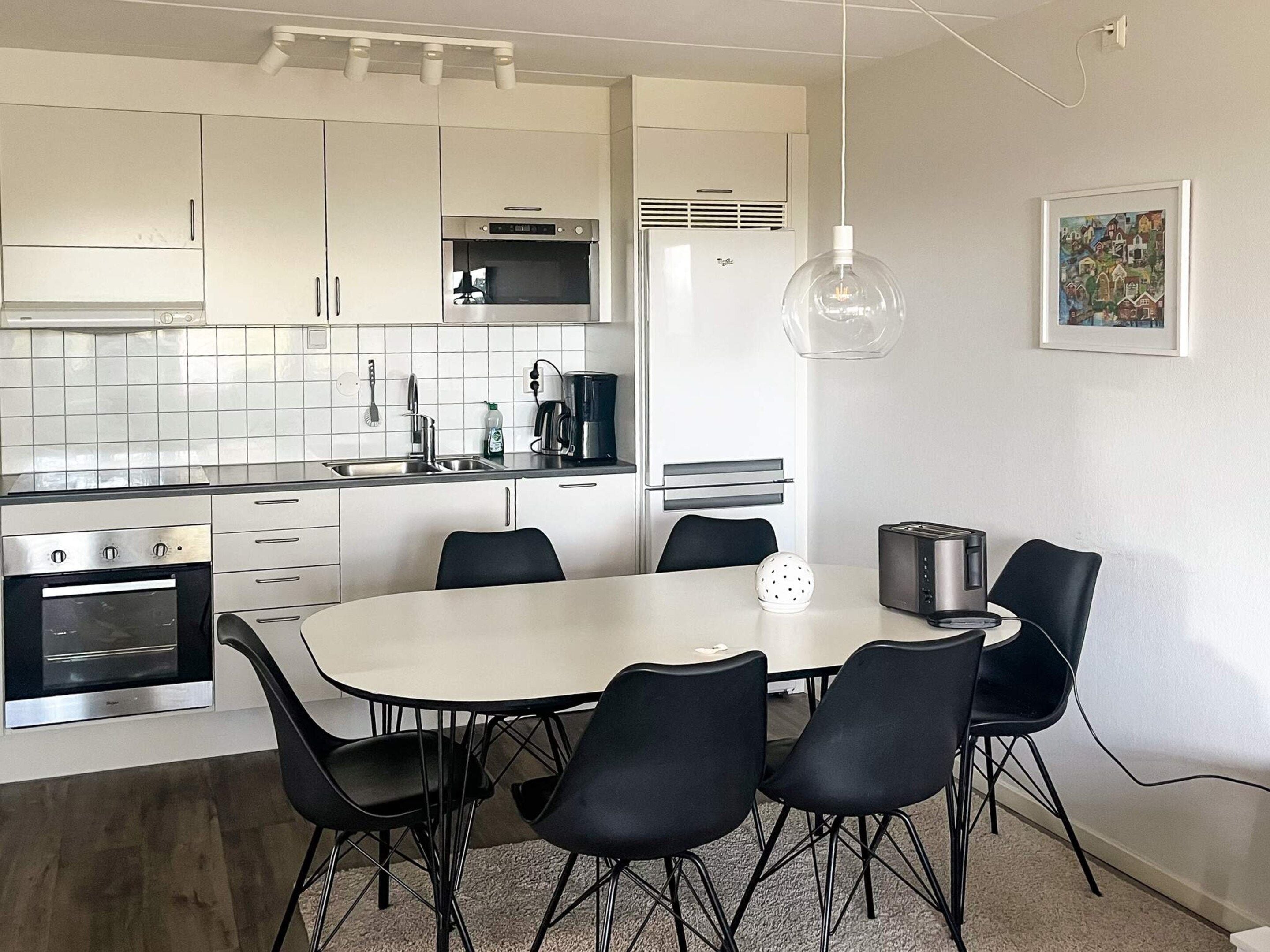 Cozinha moderna com armários brancos, micro-ondas, cafeteira e mesa de jantar com cadeiras.