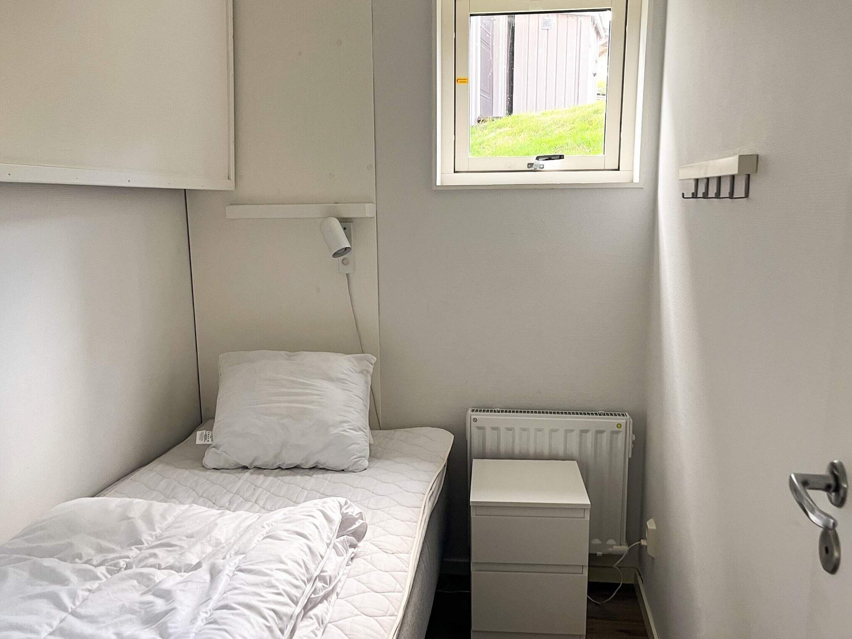 A small, single-bed room with a window, a radiator, and a bedside table.