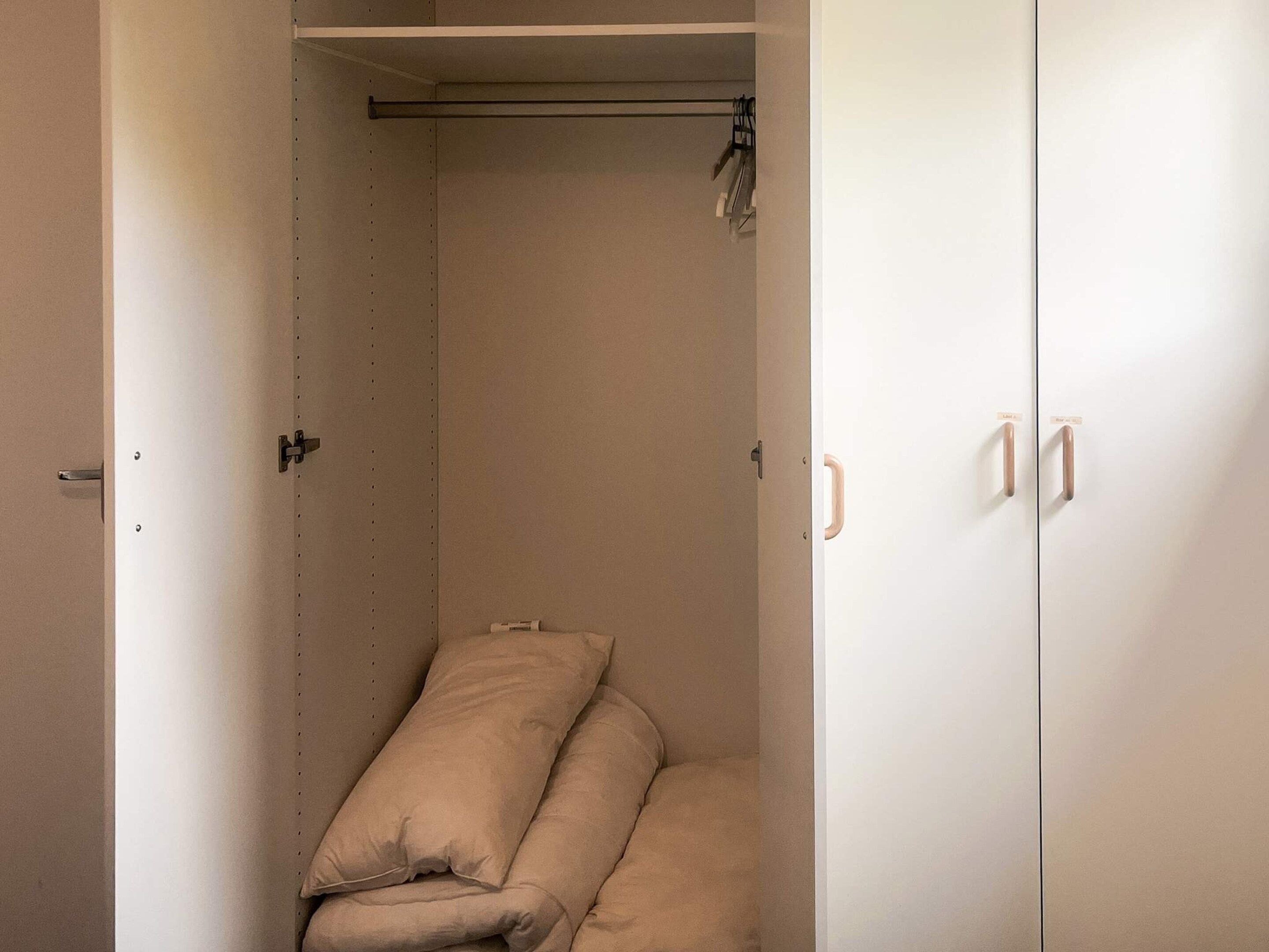Quarto pequeno e fechado, com uma cama, um guarda-roupa e uma porta.