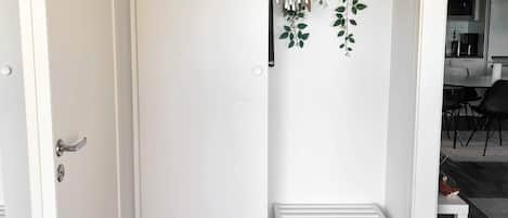 A white door with a handle, a white bench with a folded item on it, and a wall-mounted plant with hanging items.