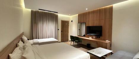 A modern hotel room with a large bed, a desk, a flat-screen TV, and a seating area.