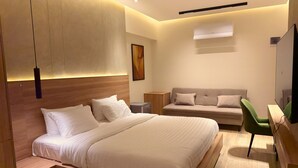 Ein modernes Hotelzimmer mit einem großen Bett, einer Sitzecke, einem Schreibtisch und einem Fernseher.