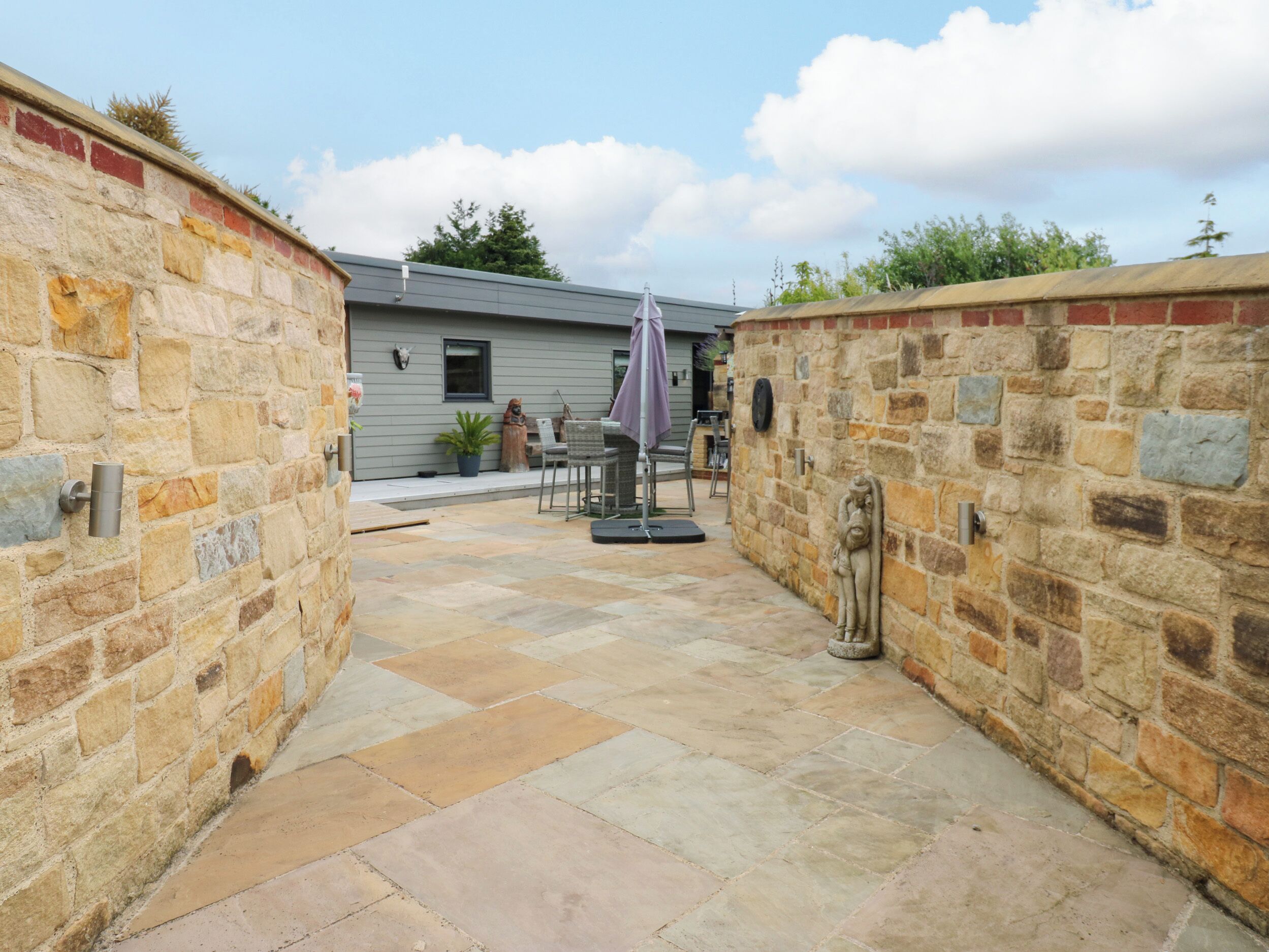 A stone-walled courtyard with a patio area, outdoor seating, and a building in the background.