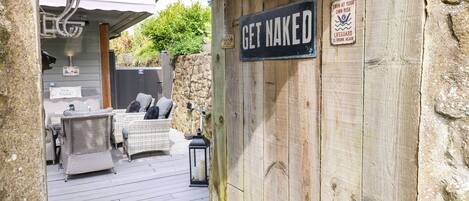 Una terraza de madera que conduce a un patio cubierto con muebles de mimbre y un letrero que dice 'GET NAKED'.