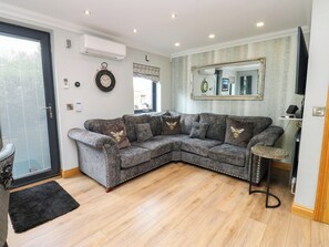 A modern living room with a grey sectional sofa, a black rug, and a wooden floor. - Caesars Lodge (Darlington)