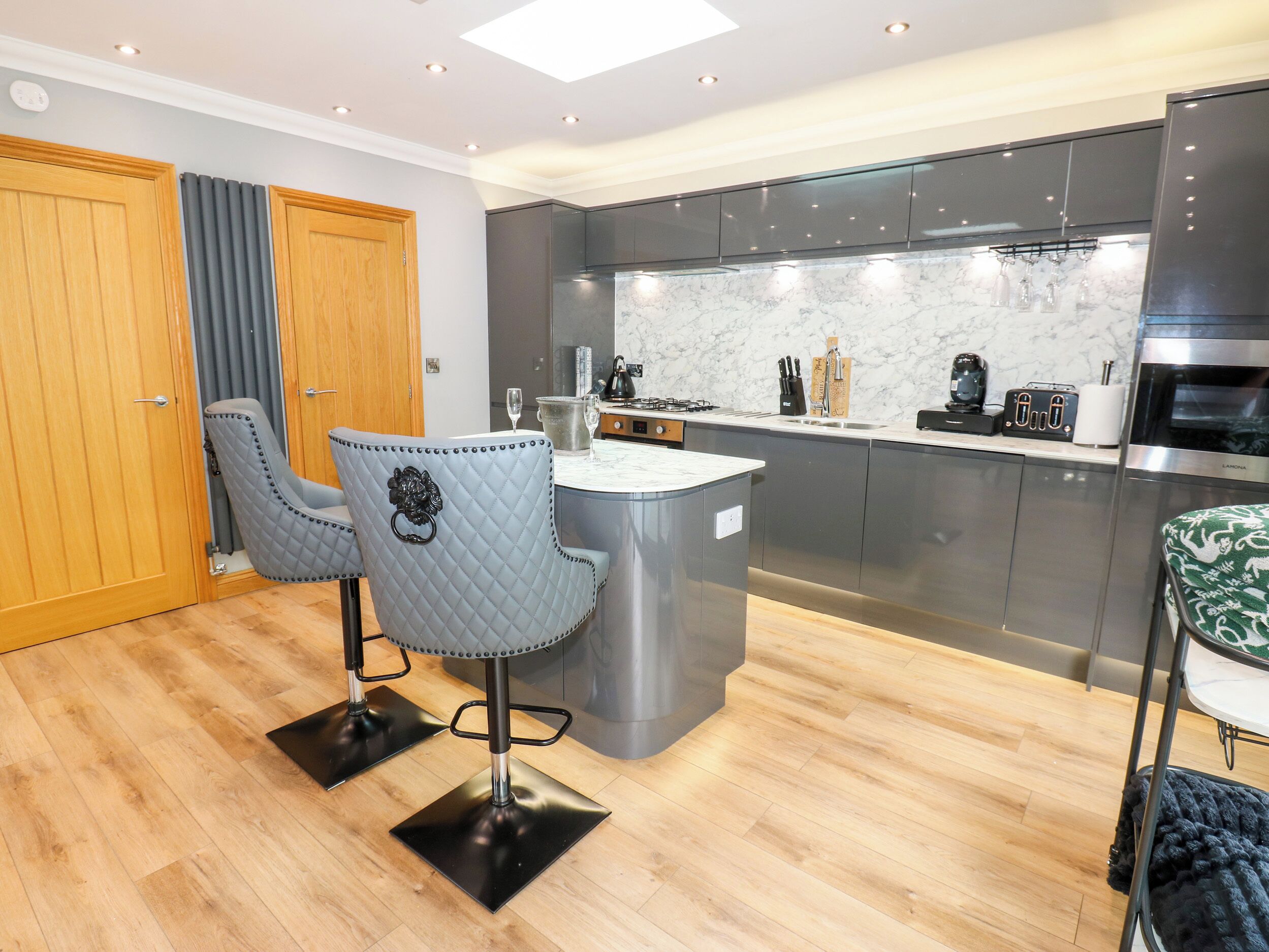 A modern kitchen with a marble countertop, dark cabinets, and a central island. There are two chairs with a quilted design.
