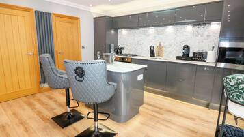 A modern kitchen with a marble countertop, dark cabinets, and a central island. There are two chairs with a quilted design.