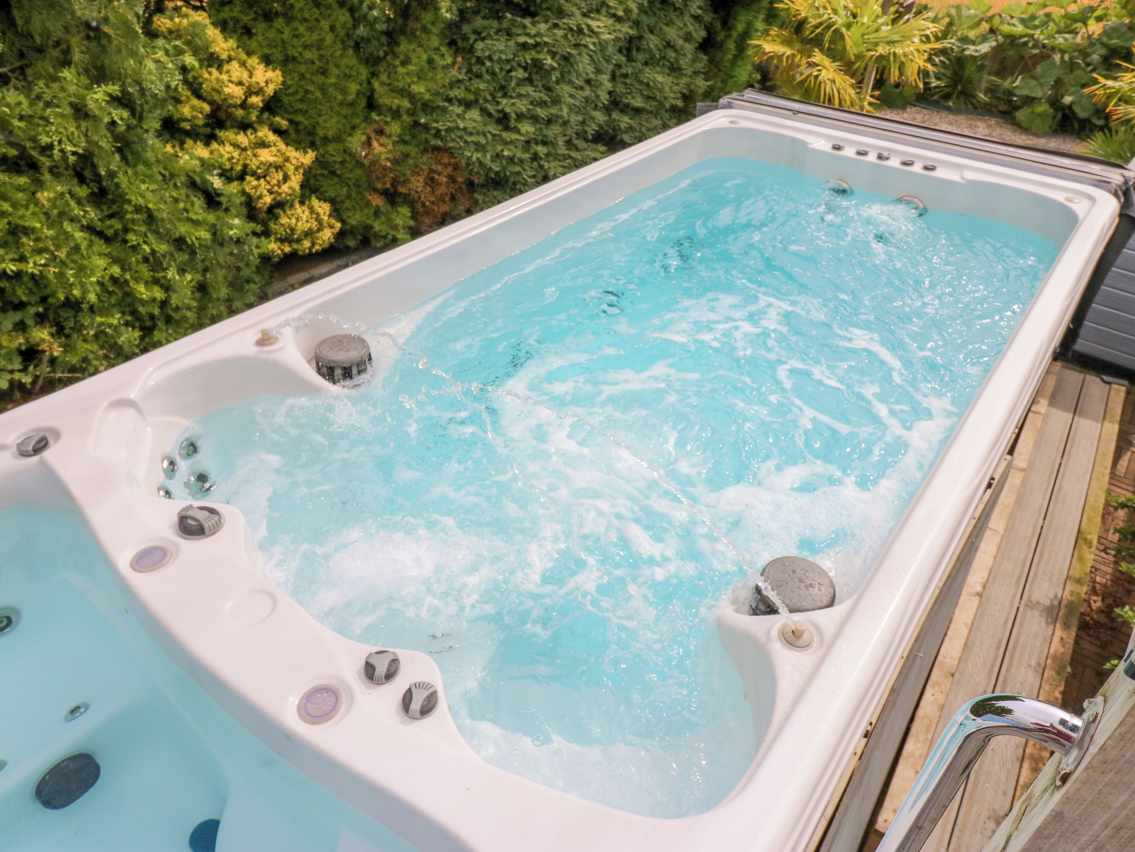 A hot tub with multiple jets, surrounded by a wooden deck and lush greenery.