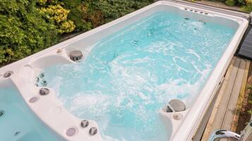 Ein Whirlpool mit mehreren Düsen, umgeben von einer Holterrasse und üppiger Vegetation.