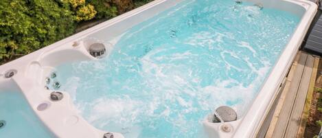 A hot tub with multiple jets, surrounded by a wooden deck and lush greenery.