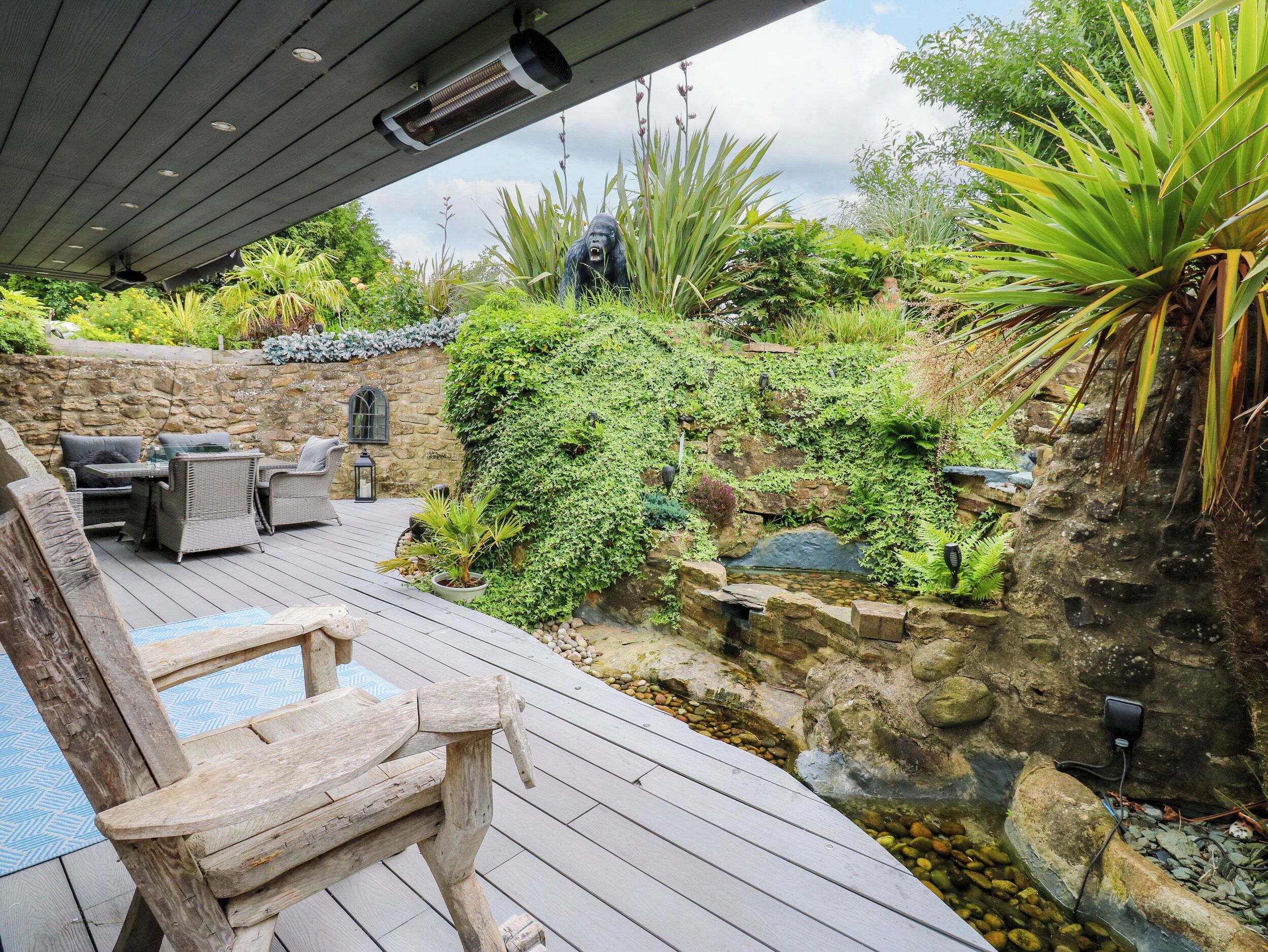 A wooden deck with outdoor furniture, a stone wall, and a small water feature.