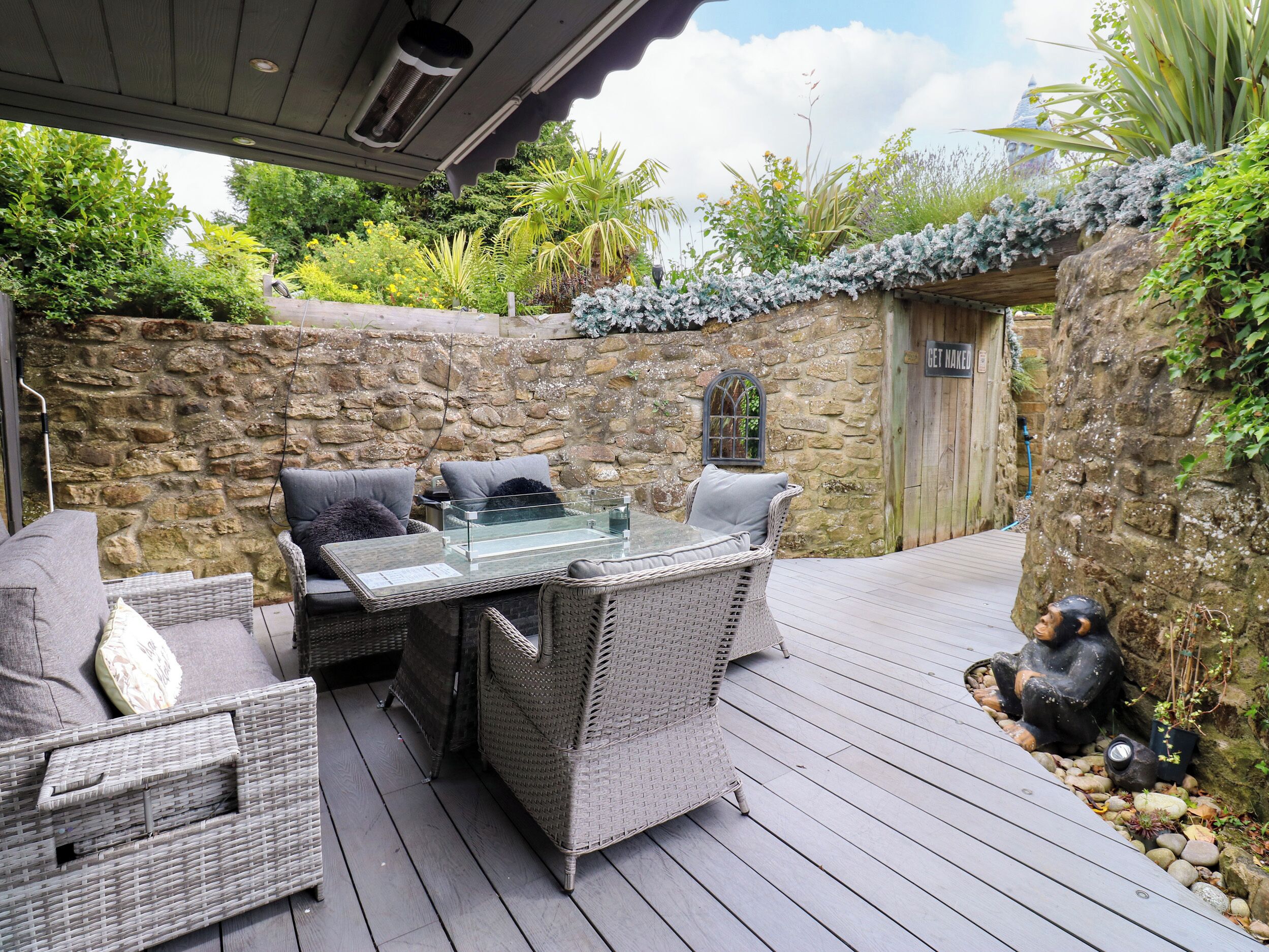 An outdoor patio with wicker furniture, a glass-top table, and a stone wall backdrop.