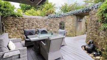 An outdoor patio with wicker furniture, a glass-top table, and a stone wall backdrop.