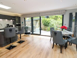 A modern kitchen with a marble countertop, a dining area with grey upholstered chairs, and a view of a lush garden through large sliding doors. - Caesars Lodge (Darlington)