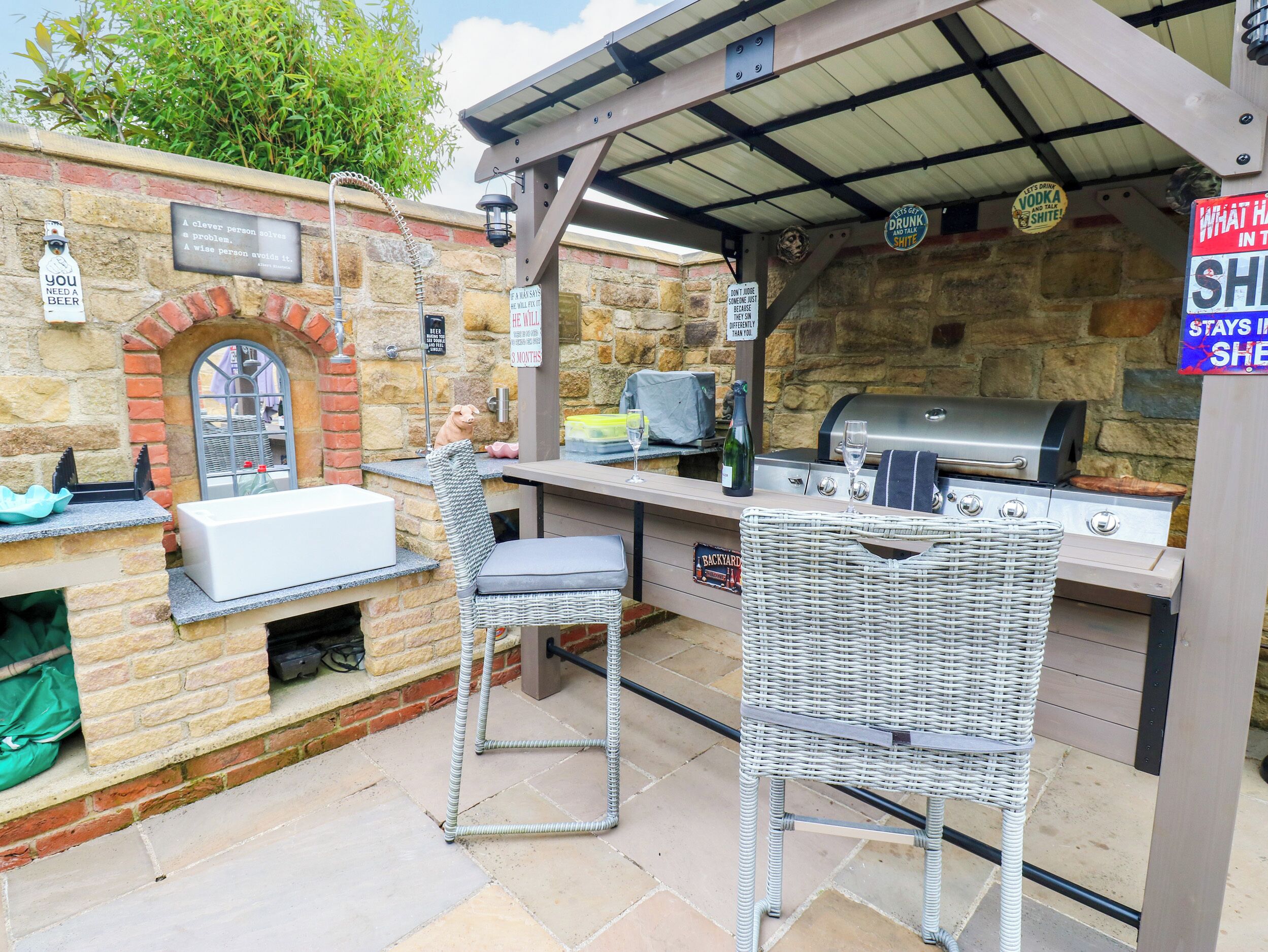 An outdoor bar area with a stone wall, a grill, and two wicker barstools.