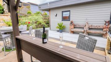 Un patio al aire libre con una mesa de madera, sillas, una botella de vino y una copa.