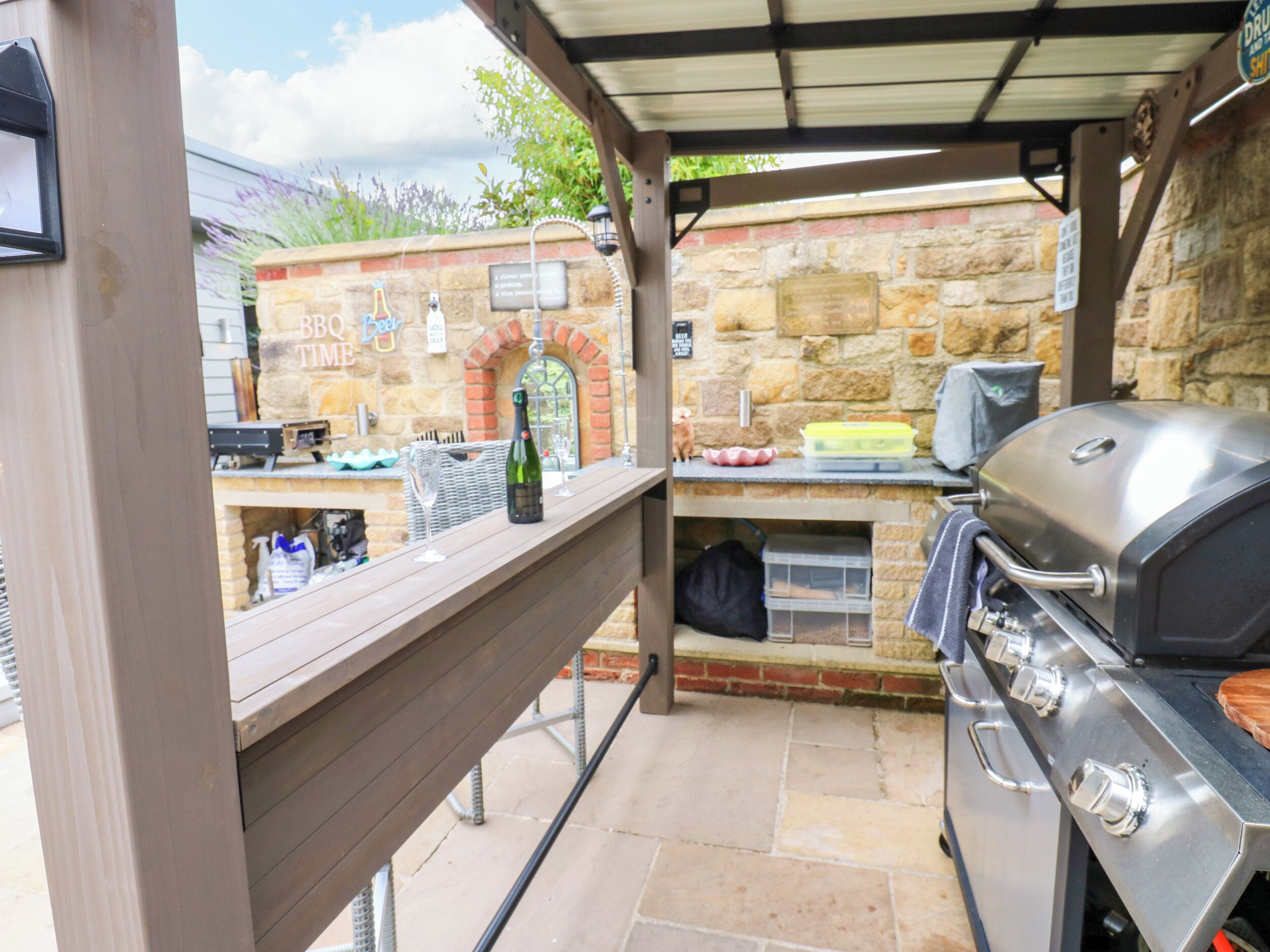 Un patio exterior con pared de piedra, una parrilla y una zona de bar con una botella de champán.