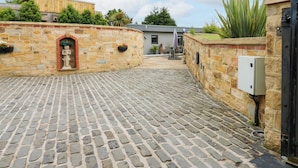 Un patio empedrado con pared de piedra, una estatua y un edificio al fondo.