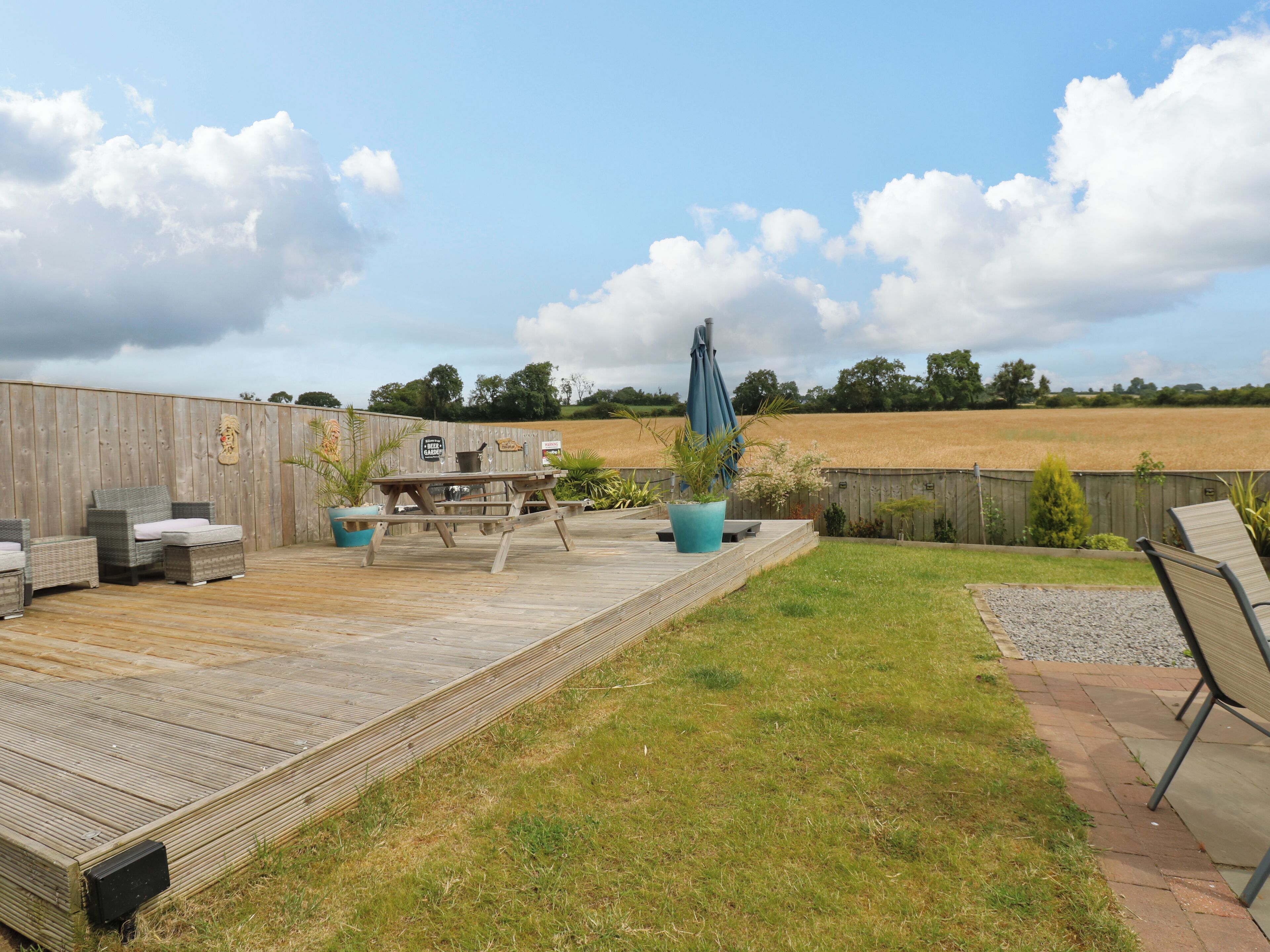 Une terrasse en bois avec des meubles d’extérieur, une table de pique-nique et une vue sur un champ.