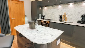 Una cocina moderna con encimera de mármol, estufa integrada y muebles oscuros.