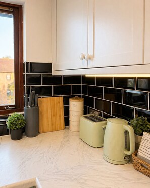 A kitchen with white cabinets, black tiled backsplash, a wooden cutting board, a knife holder, a toaster, a kettle, and two containers labeled 'tea' and 'coffee'. - Cozy stay in city centre with free parking (Edinburgh)