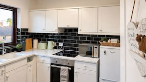 Una cucina moderna con mobili bianchi, zoccolo a mosaico nero, forno integrato e frigorifero.