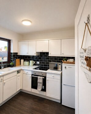 A modern kitchen with white cabinets, a black tiled backsplash, a built-in oven, and a refrigerator. - Cozy stay in city centre with free parking (Edinburgh)