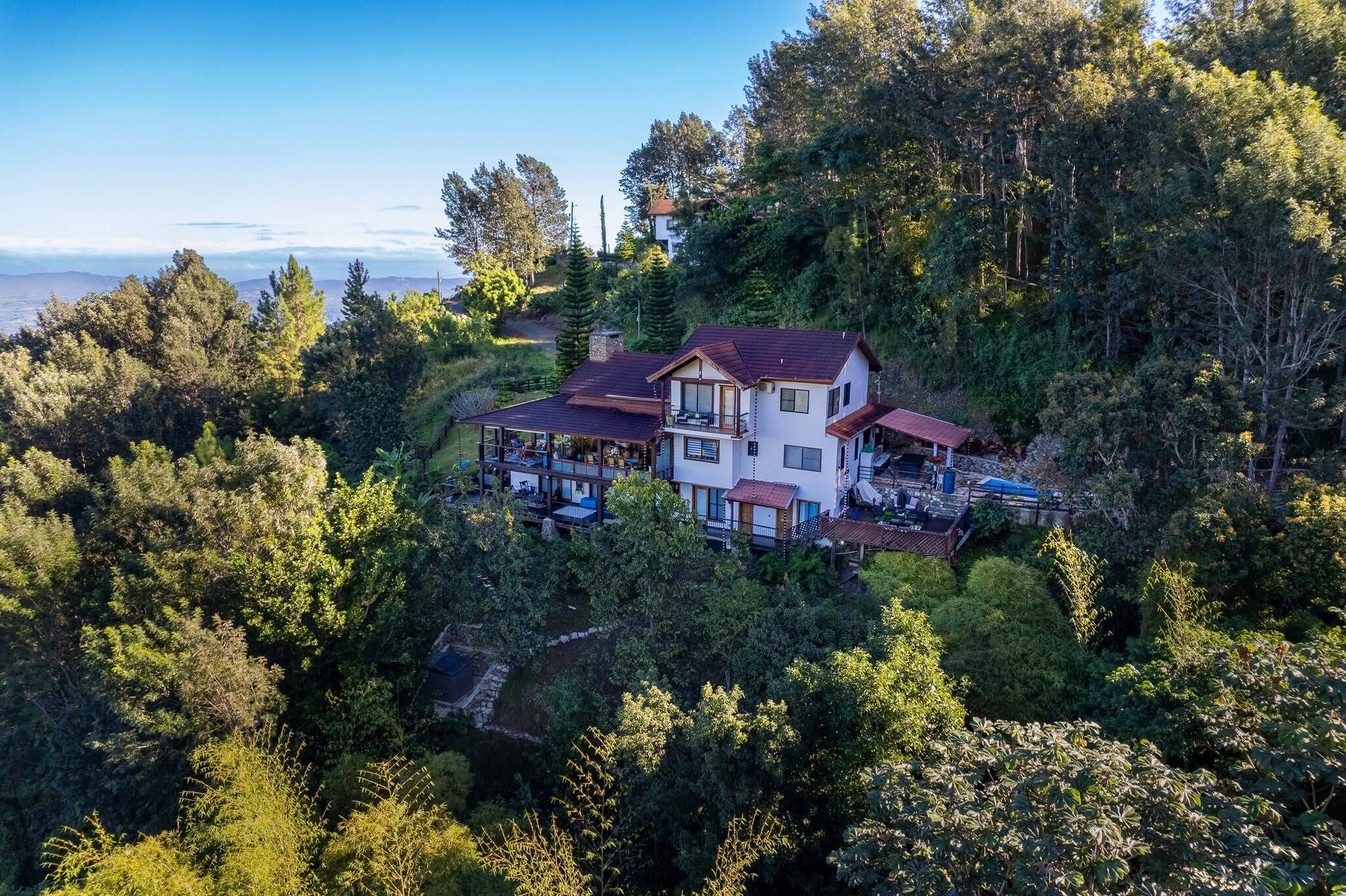 A large house surrounded by dense forest, with multiple levels and a prominent balcony.