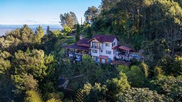 A large house surrounded by dense forest, with multiple levels and a prominent balcony.