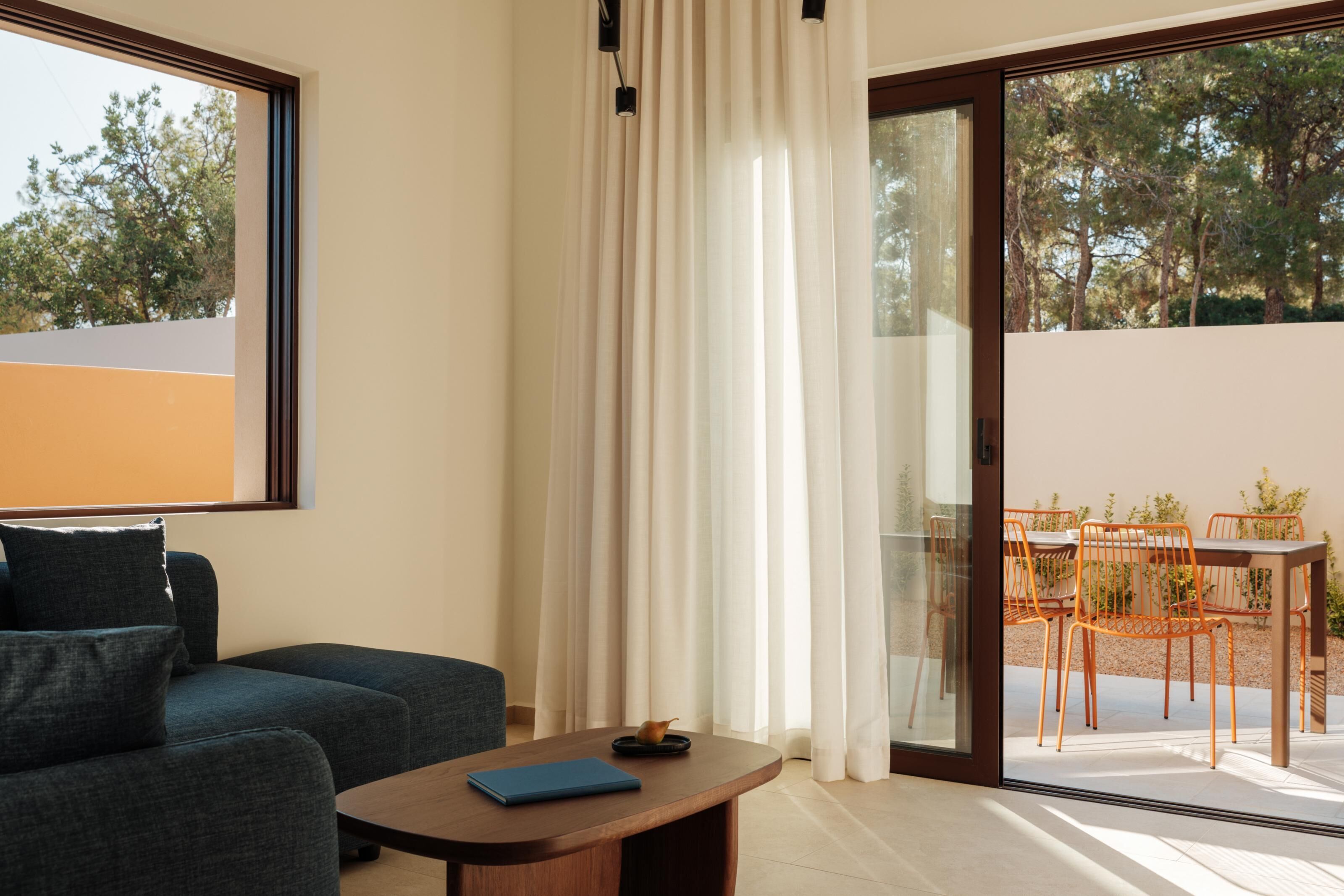 Een moderne woonkamer met een bank, een salontafel en een schuifdeur naar een terras buiten met een tafel en stoelen.