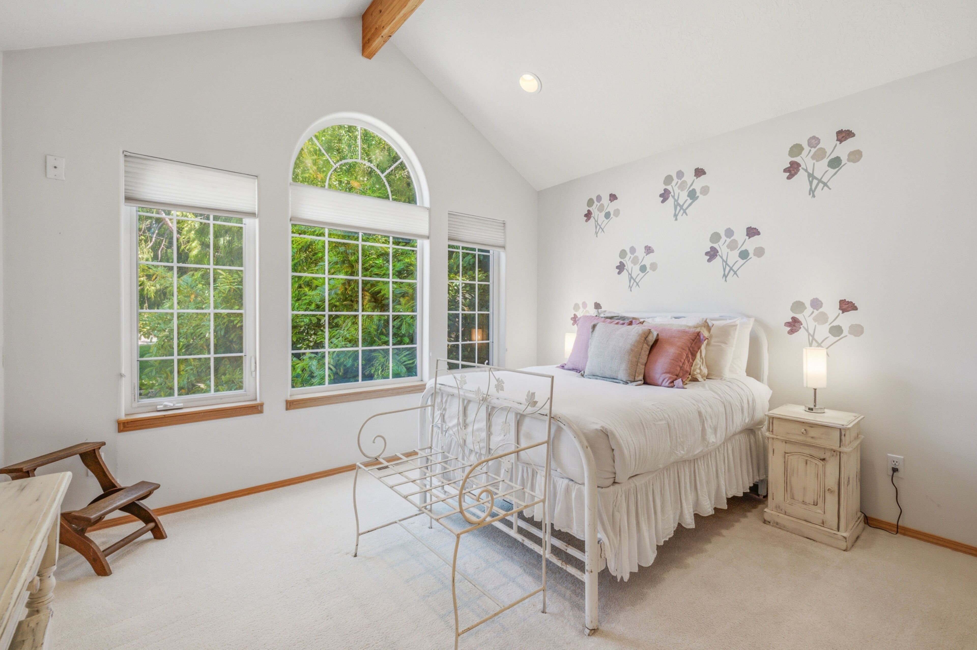 A bedroom with a bed, a nightstand, a window with a view of greenery, and a bench.