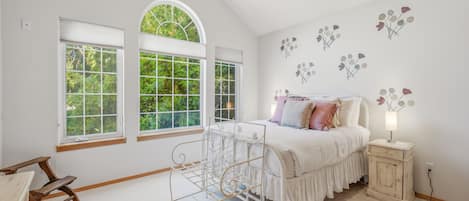 A bedroom with a bed, a nightstand, a window with a view of greenery, and a bench.