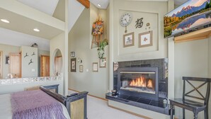 Een kamer met een open haard, ingelijste foto's, een klok en een televisie.