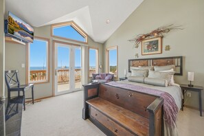 A bedroom with a large bed, a bench, a TV, and a balcony with a view.