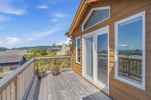 A wooden deck with potted plants, large windows, and a view of a hilly landscape. - Panoramic Ocean Views, Grill, Wraparound Decks (Pacific City)