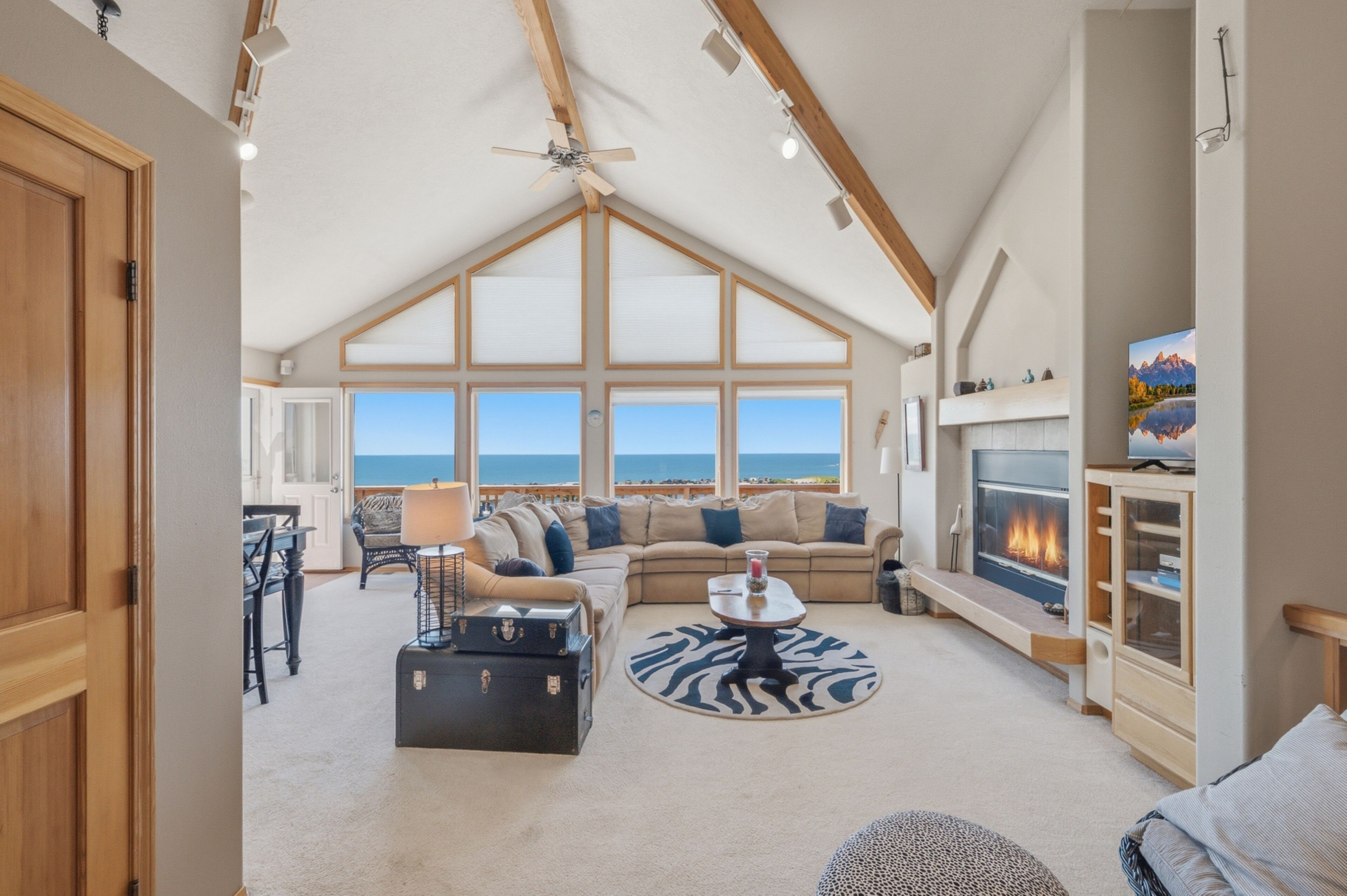 A spacious living room with a high ceiling, large windows offering a view of the ocean, a fireplace, and a cozy seating area.