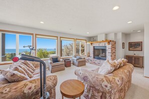 A spacious living room with a fireplace, large windows, and a view of the sea. - Panoramic Ocean Views, Grill, Wraparound Decks (Pacific City)