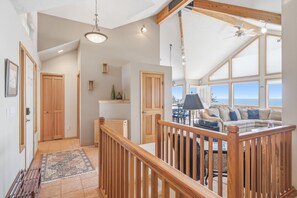 A spacious living area with a high ceiling, wooden beams, a view of the sea, and a cozy seating arrangement.