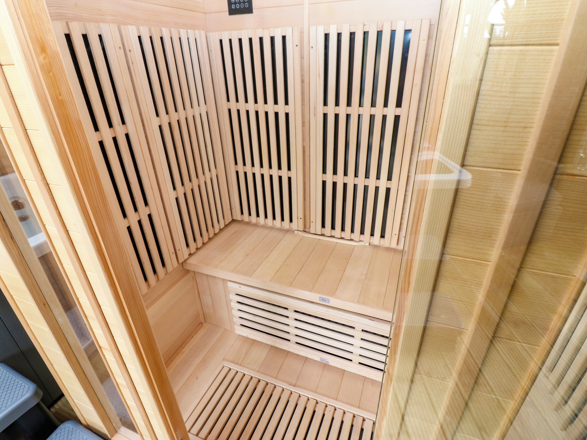 A sauna room with wooden slats, a bench, and a vent.