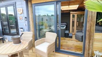 Una terraza de madera con mobiliario de mimbre y un portón de cristal que da a un patio.